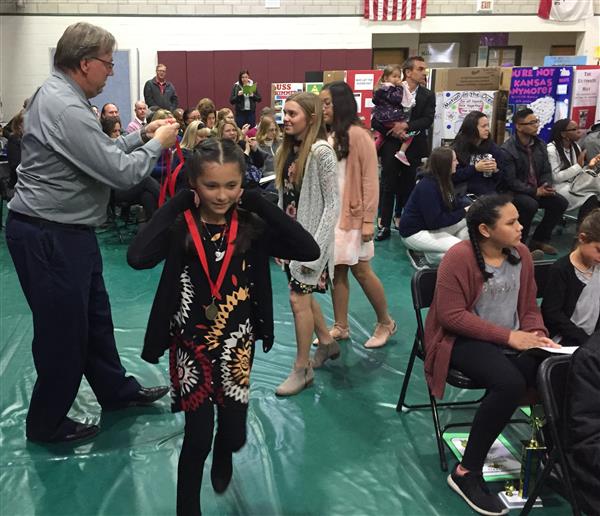 Assistant Principal Stephen Buss gets ready to place a ribbon around a female student's neck.